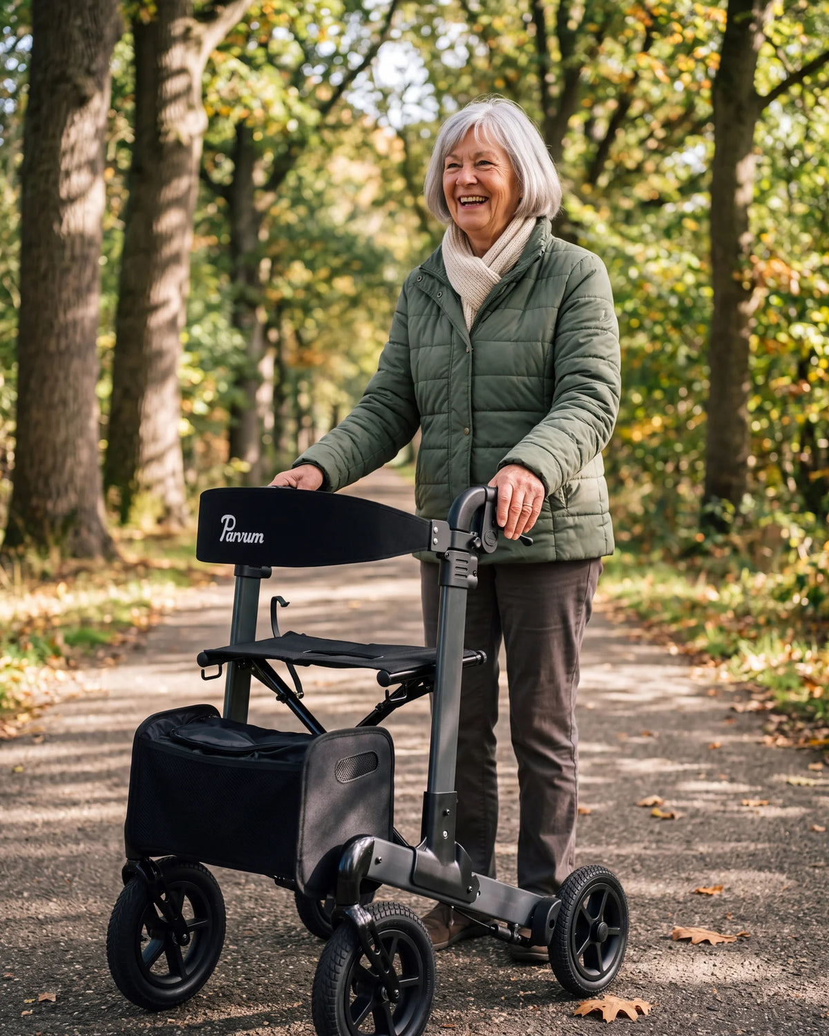Parvum Luxo Air in antraciet onder eikenbomen; een vrouw met grijs haar lacht, haar handen op de handvatten.
