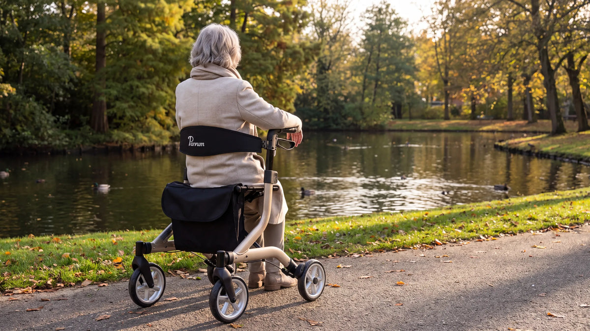 Parvum SuperLight in champagne aan een vijver in het park; een vrouw met grijs haar zit op de rollator, rug tegen de rugleuning.