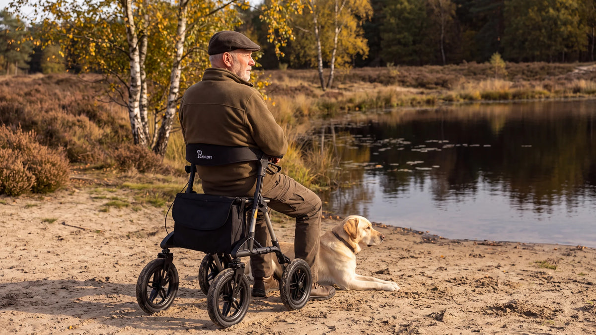 Parvum Rebel in grijs aan een heideven; een man zit op de rollator, zijn labrador ligt naast hem.